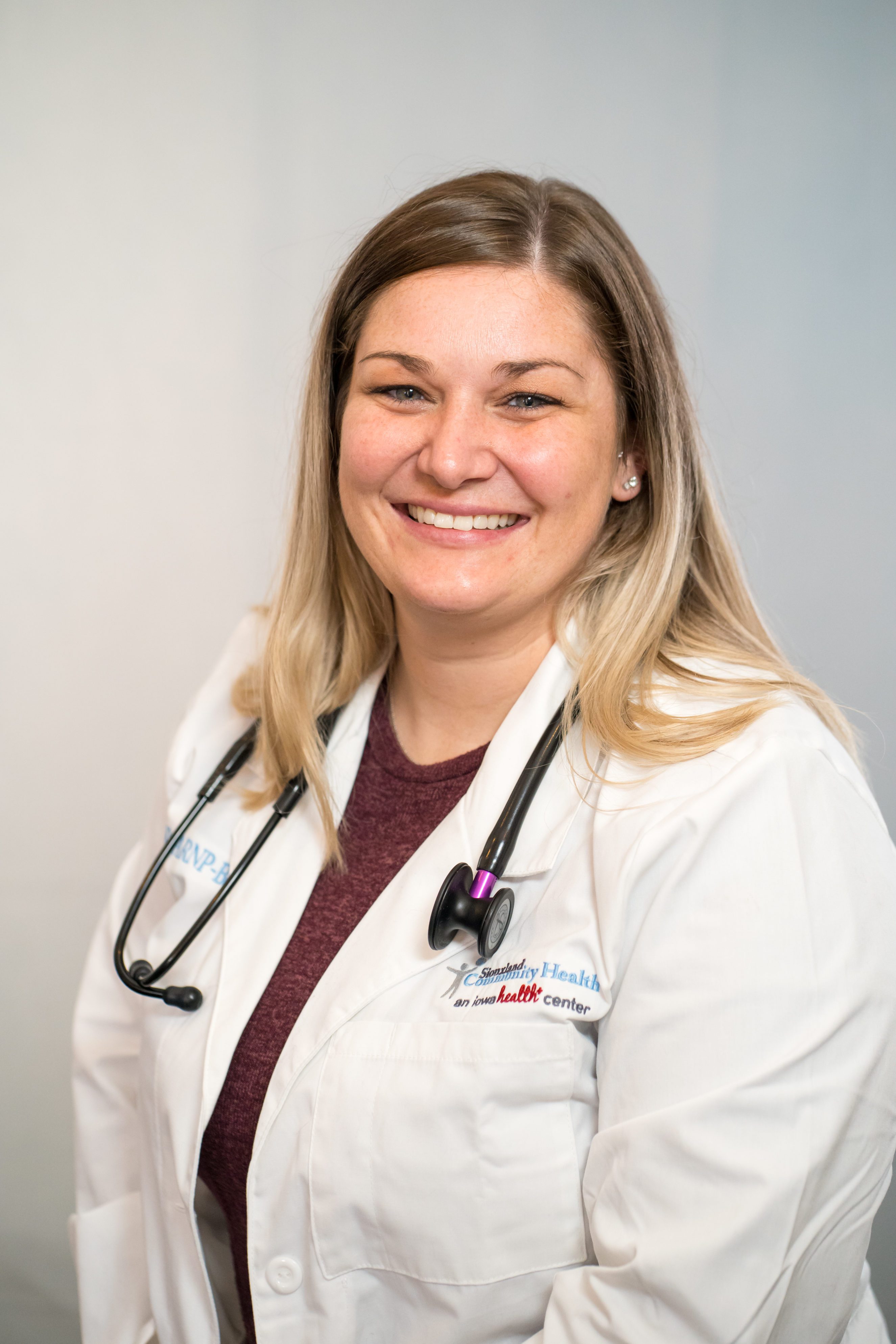 DENTAL_Ashley Huber, DDS Smiling brunette woman with red glasses and white dentist coat.